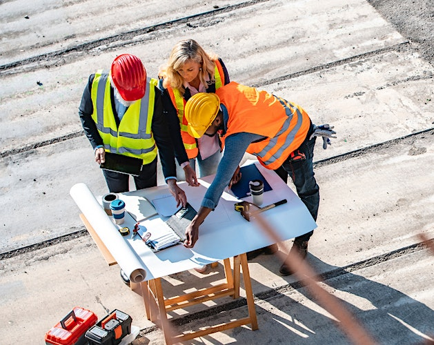 Pictured: 3 people overhead drafting table reviewing construction plans